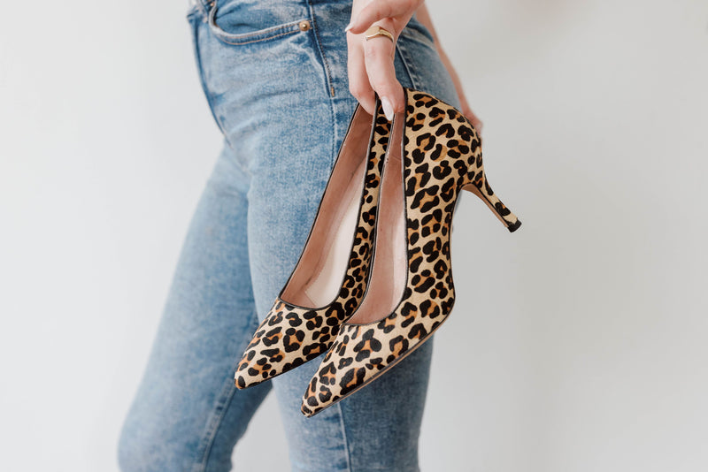 A person holding leopard print high heels while wearing blue jeans.